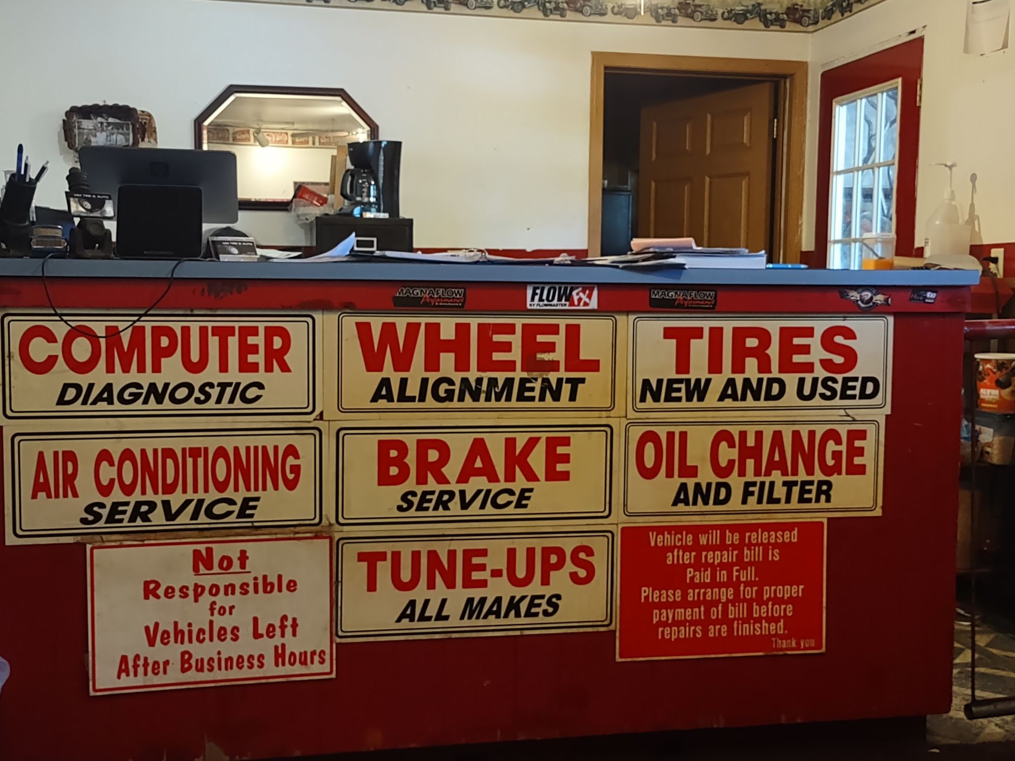 The front counter inside MM Tire & Auto, lined with painted service signs for tires, brakes, alignment, oil changes and tune-ups